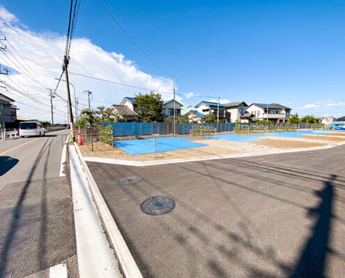 新築戸建て住宅の分譲地「ラシット横浜 汲沢町 全12棟」の現地入り口。舗装された道路とブルーシートで覆われた区画が見える。