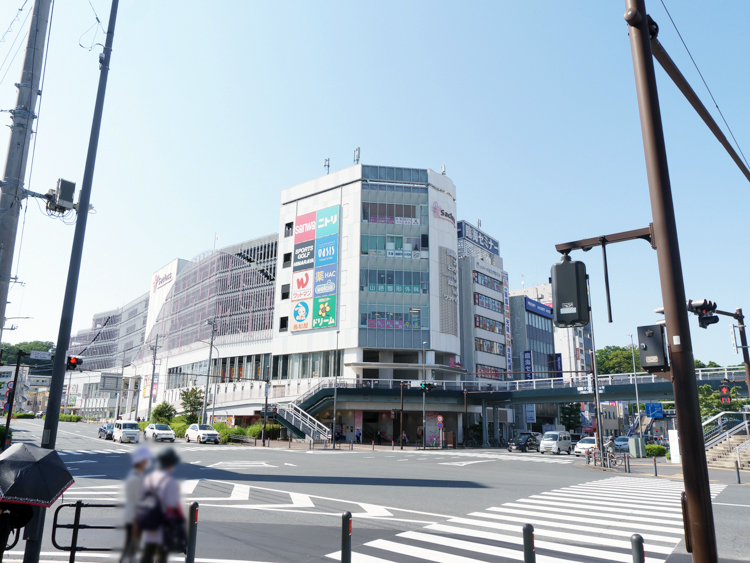 戸塚駅西口に位置するショッピングモール『サクラス戸塚』の外観。現代的なデザインのビルで、大きなガラス窓と明るい看板が特徴。建物の前には広い歩道と、周囲にある他の商業施設やバス停が見え、賑やかな駅前の風景が広がっている。