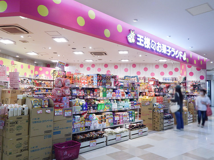 サクラス戸塚にあるお菓子屋さん『王様のお菓子ランド』の店頭。カラフルな看板とディスプレイが目を引き、ショーウィンドウには様々な種類のお菓子が美しく並べられている。