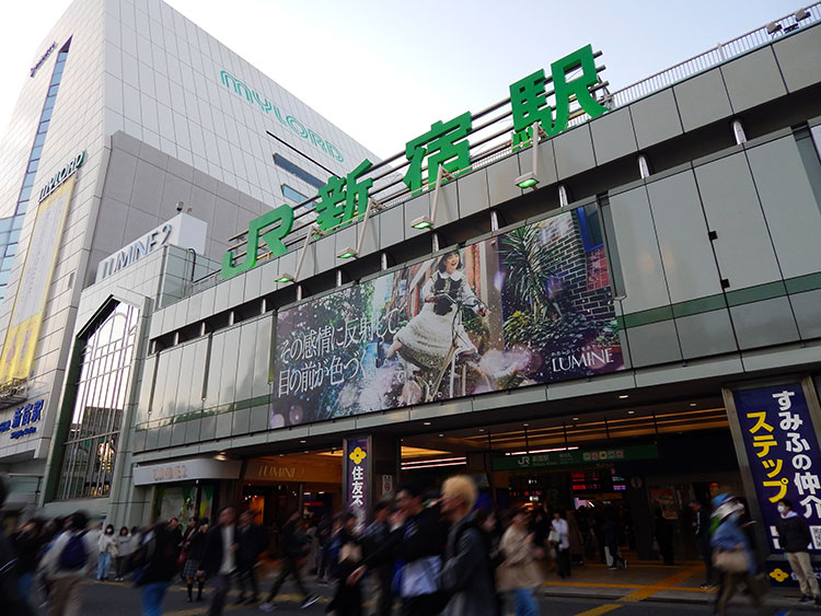 巨大な駅名が目を引くJR新宿駅南口。夕刻間近で多くの人々が行き交う様子が見える。